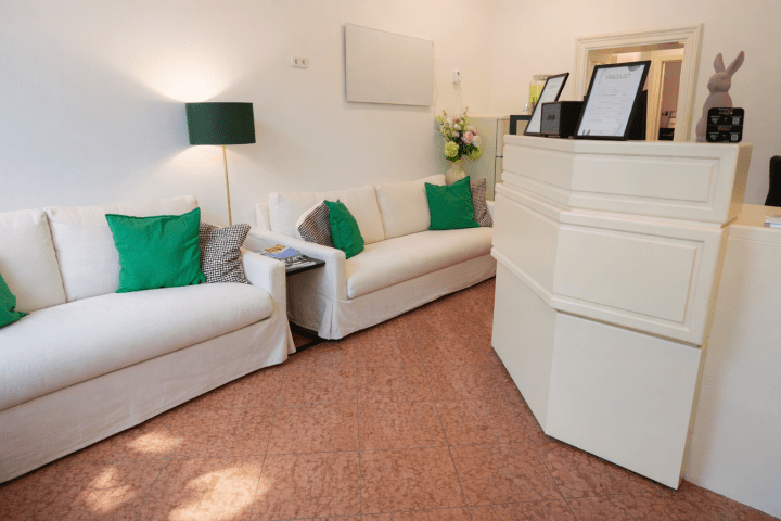 Reception area with white sofas, green pillows, and a white counter.