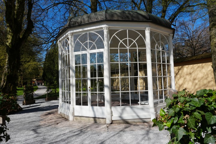 A white, octagonal gazebo with glass windows in a park setting.