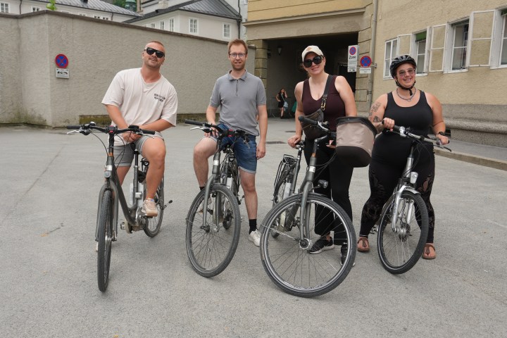 Four people with bikes posing on a street, smiling.