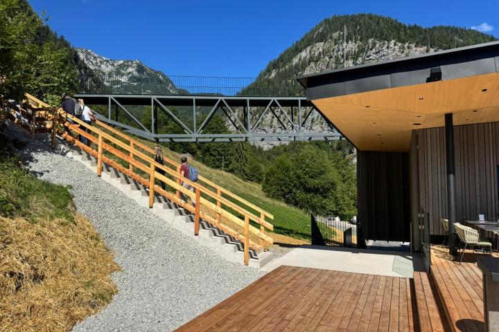 People walking up stairs near modern building with mountainous background.