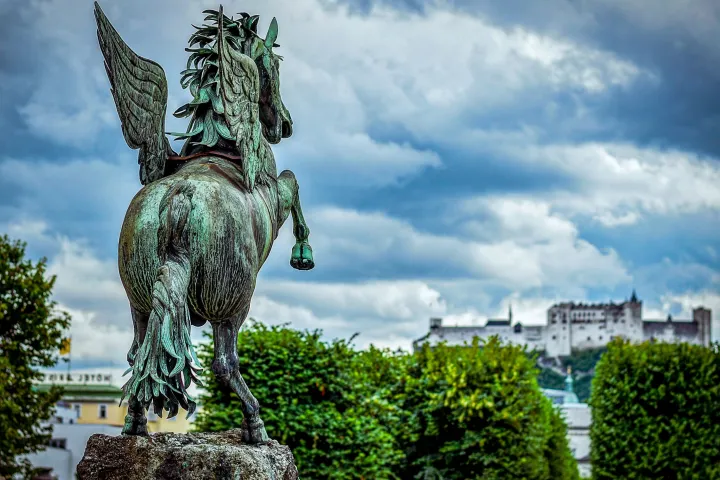 Bronze Pegasus statue with castle and cloudy sky background.