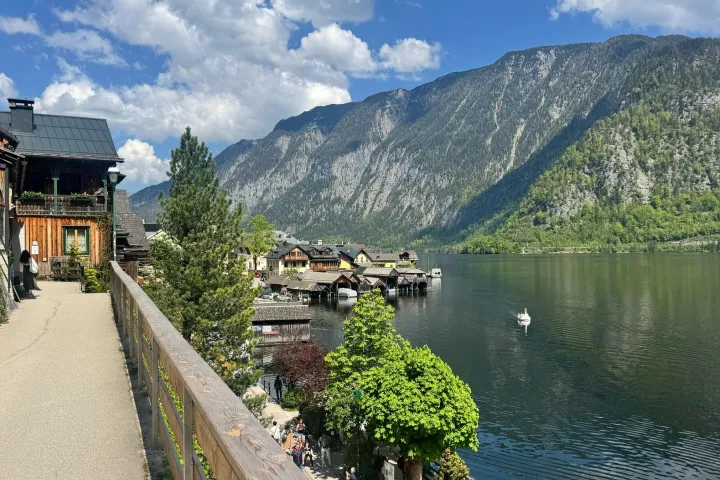 a train is parked on the side of a river with Hallstatt in the background