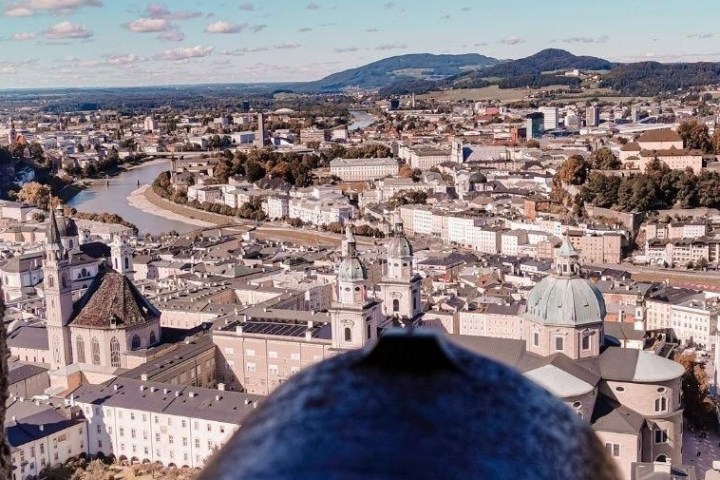 Aerial view of a European city with a river, historic buildings, and distant hills under a cloudy sky.