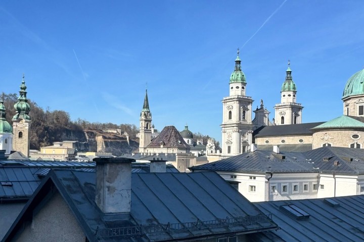 Skyline of a historic city with multiple church towers and domes against a clear blue sky.