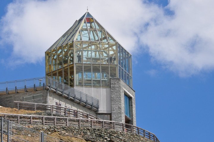 Glass observatory with stone base on hill against blue sky with clouds.
