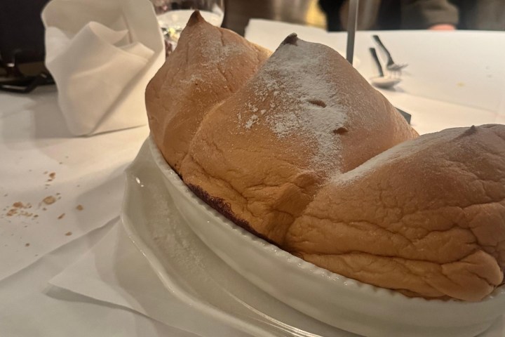 Large, fluffy pastry on a dish with sugar dusting on a tablecloth.