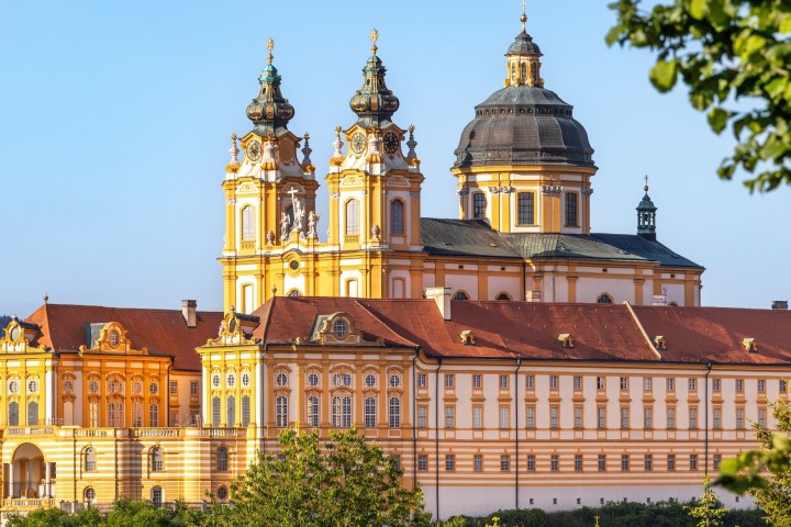 Baroque-style abbey with yellow walls, twin towers, and dome under a clear blue sky.