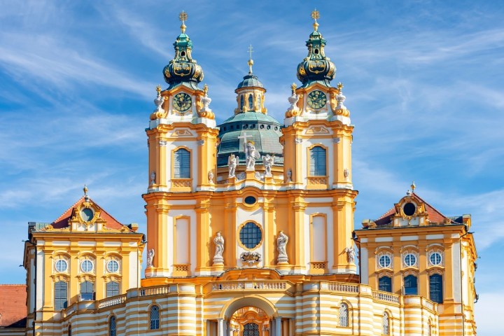 Baroque-style abbey with twin towers and statues against a blue sky.
