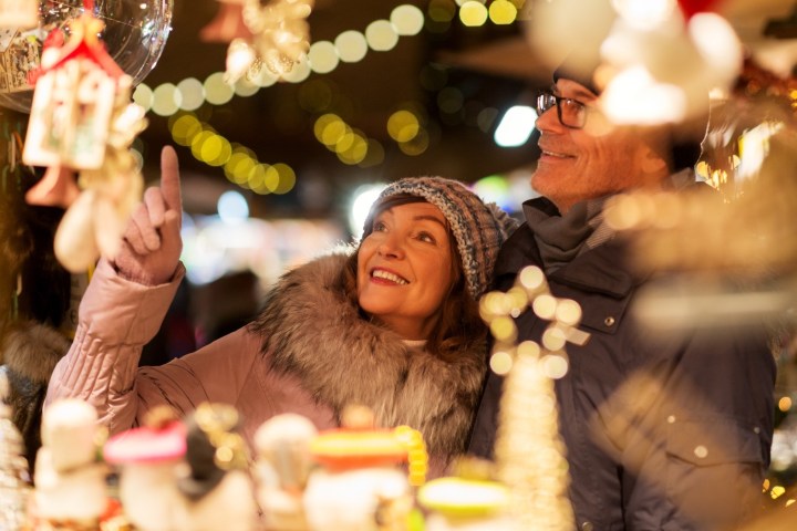 Smiling couple in winter clothes admire Christmas decorations at a festive market.