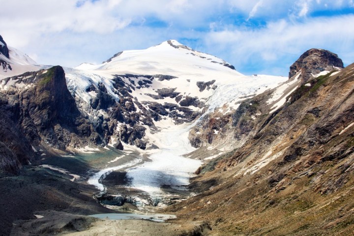 Snow-capped mountain and glacier in rocky valley under partly cloudy sky.