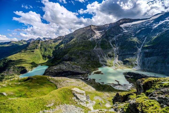 Mountain landscape with green valleys and turquoise lakes under a blue sky with clouds.