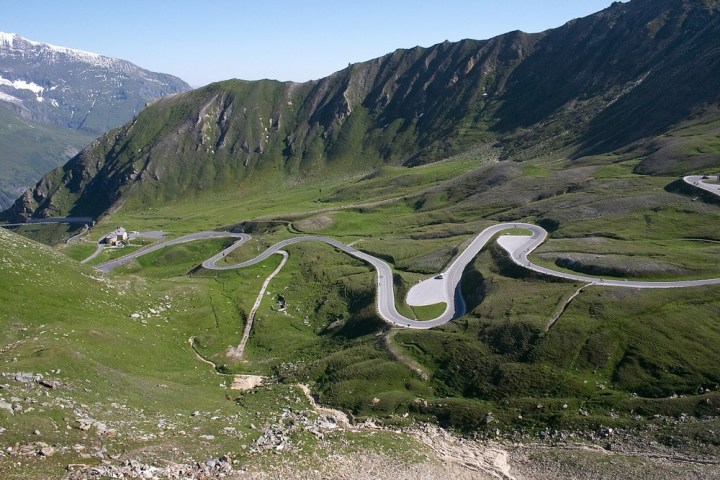 Winding mountain road with sharp curves in a green valley under a blue sky.