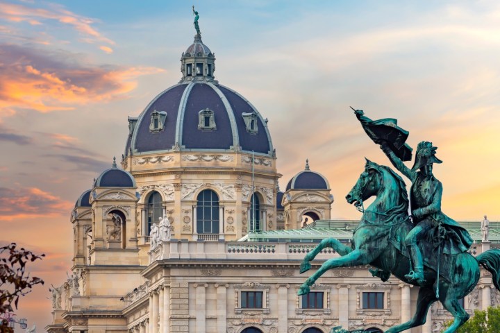 Dome of a historic building with a bronze equestrian statue in front, during a colorful sunset.