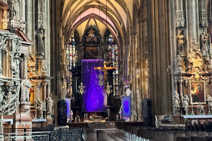 Ornate cathedral interior with statues, stained glass, and a purple drape at the altar.