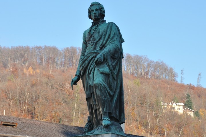 Statue of a historical figure with trees and a clear sky in the background.
