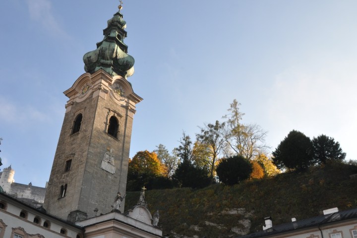Tall church tower with green dome against blue sky, trees in background.