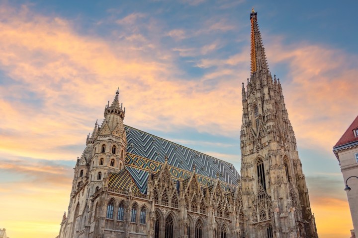 Gothic cathedral with colorful roof under a sunset sky with clouds.