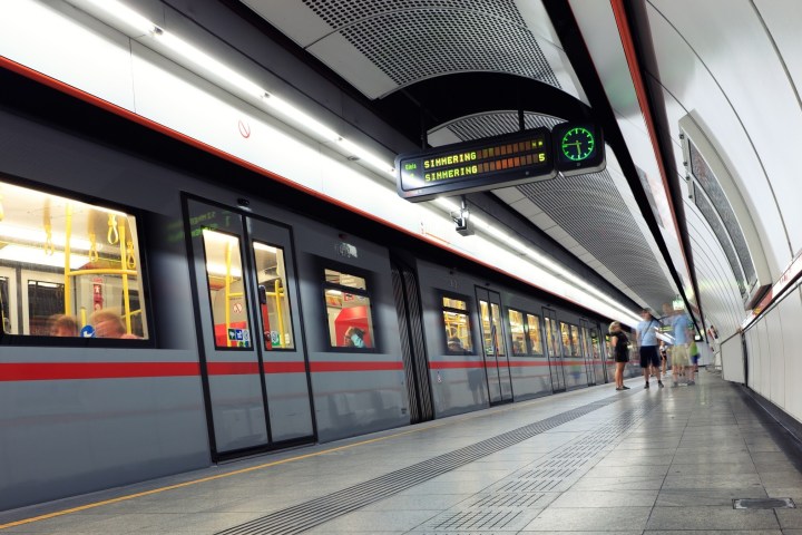 Subway train at a station platform with passengers and digital display overhead.