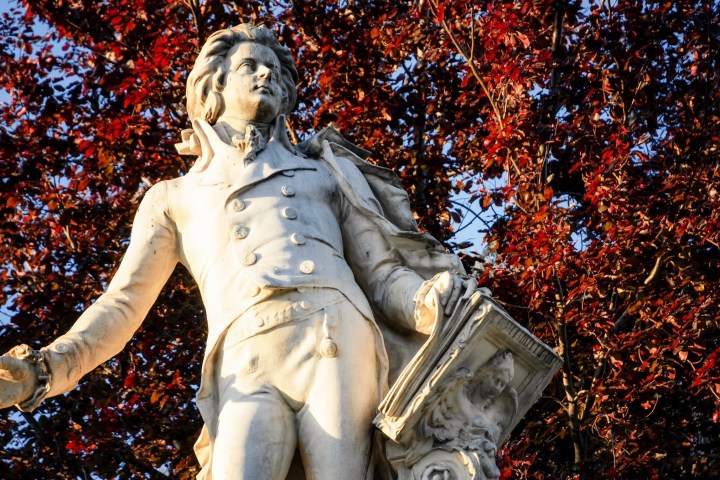 Statue of a man in historical attire with red-leaved trees in the background.
