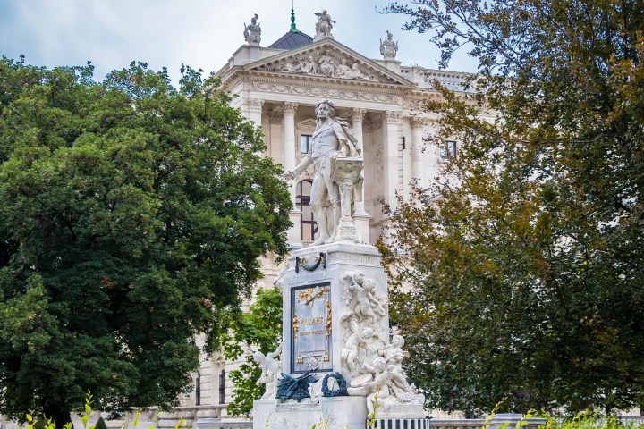 Statue surrounded by trees in front of a neoclassical building.