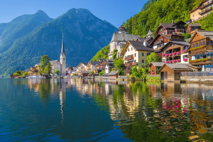 Scenic lakeside village with church steeple, colorful houses, and mountain backdrop.