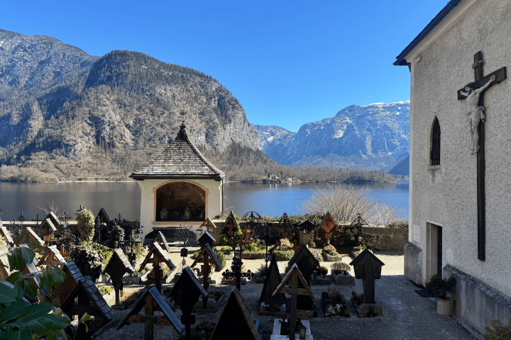 Gravestones and chapel by a lake with mountains in the background.