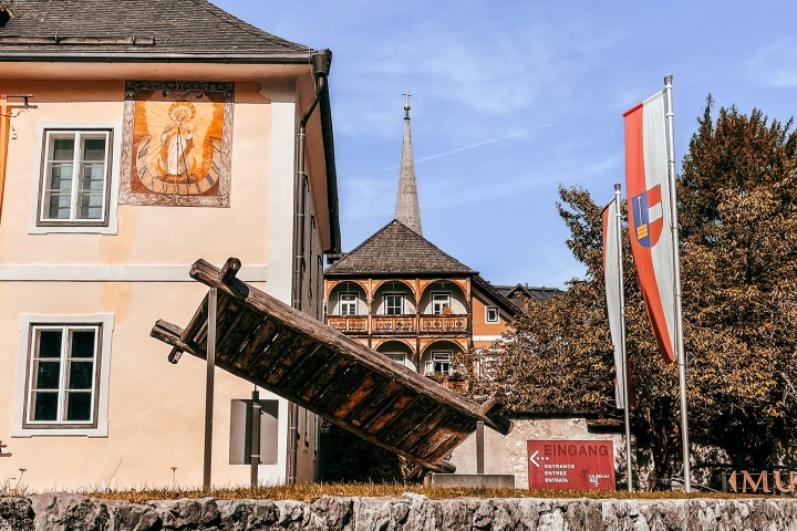 Historic building with mural, wooden sculpture, flags, and entrance sign in a scenic area.