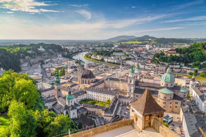 Panoramic view of Salzburg, Austria with historical buildings, a river, and surrounding hills under a blue sky.