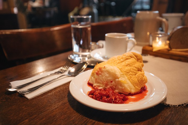 Dessert on plate with berry sauce, glass of water, and coffee on a wooden table.