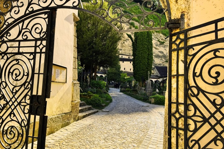 Ornate wrought iron gate opening to a cobblestone path in a garden.