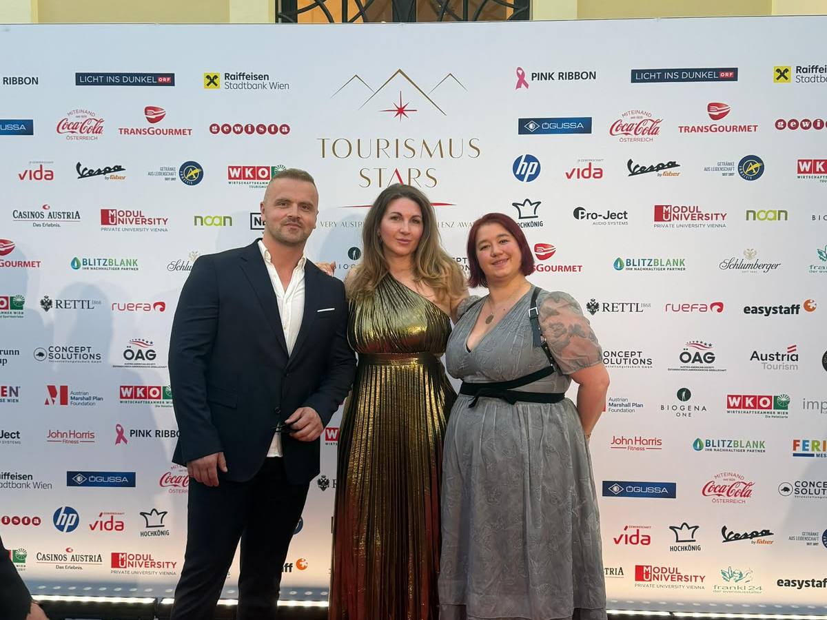 Three people pose on red carpet in front of a backdrop with logos.