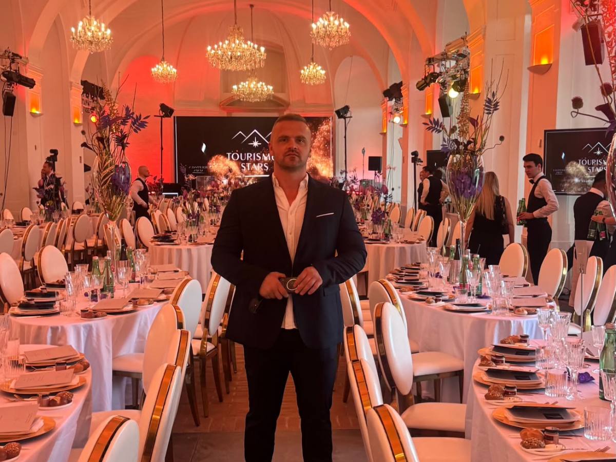Person in suit stands in elegant event hall with decorated tables.